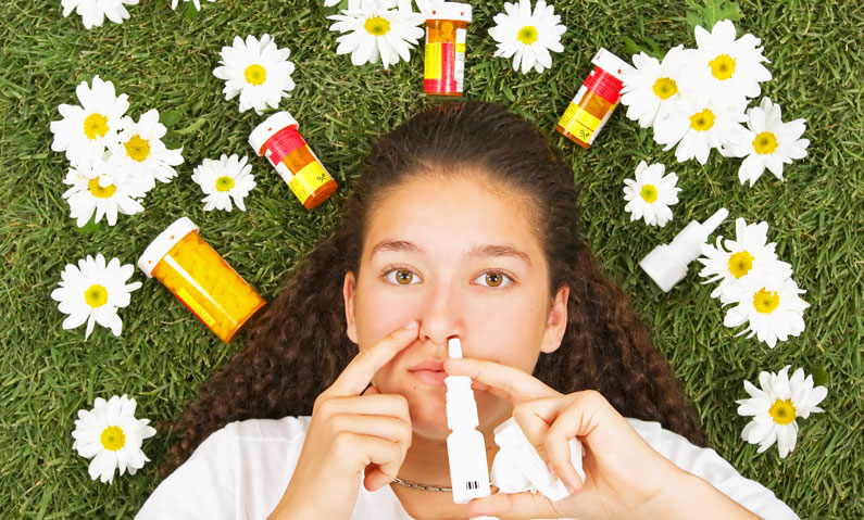 Kvinde med allergi mellem blomster på en græsplæne tager allergimedicin